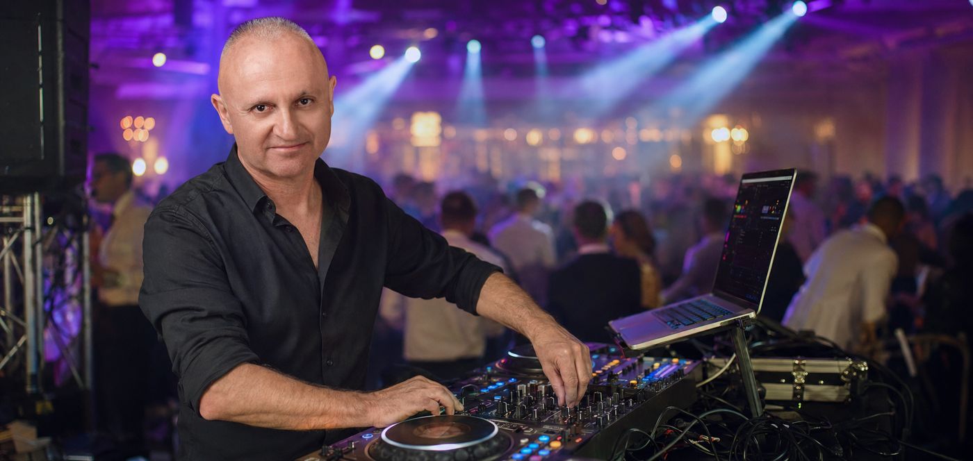 DJ Przemo przy konsolecie w trakcie zabawy weselnej, tłum gości w tle
