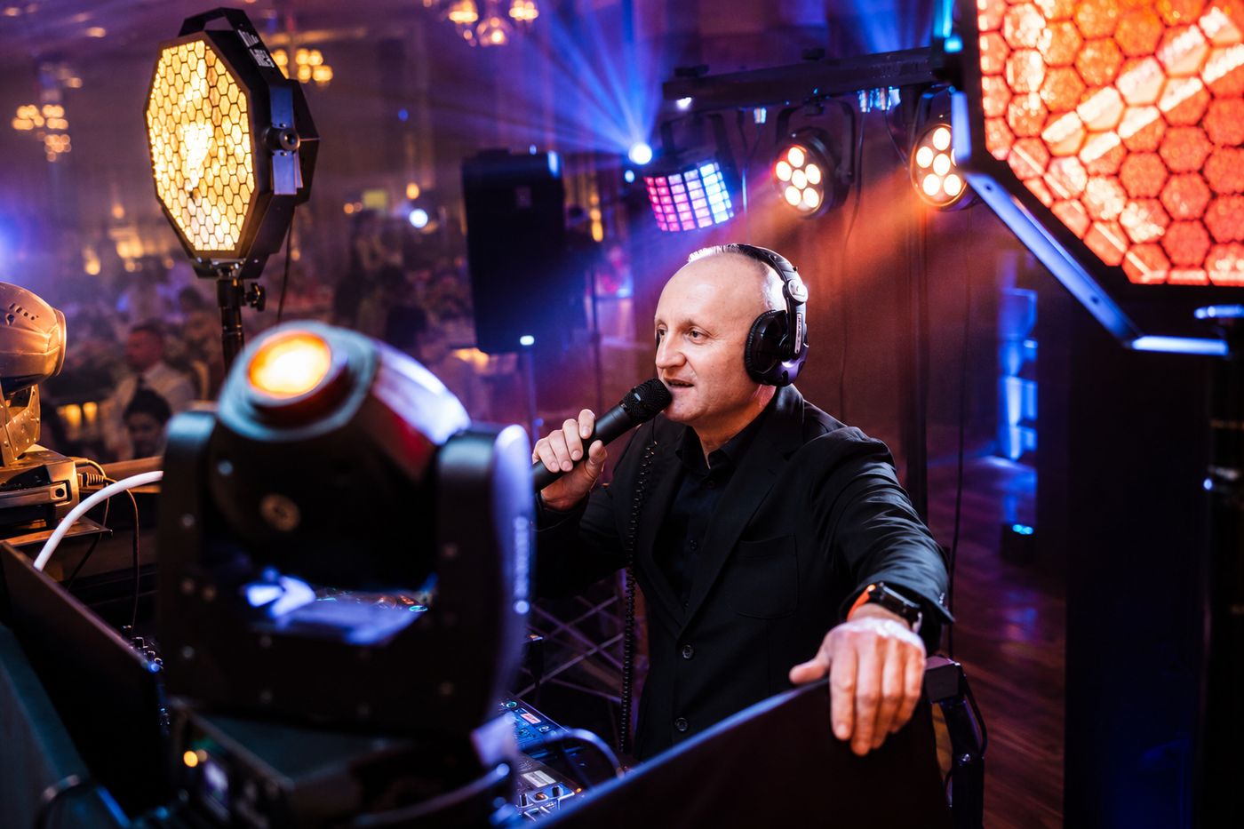 DJ Przemo z mikrofonem, efektowne oświetlenie w tle podczas prowadzenia imprezy