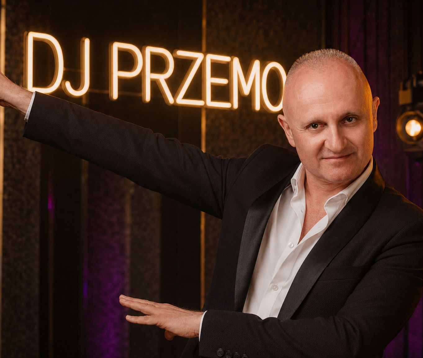DJ Przemo Gadomski pozujący przy świetlnym neonem z napisem DJ PRZEMO